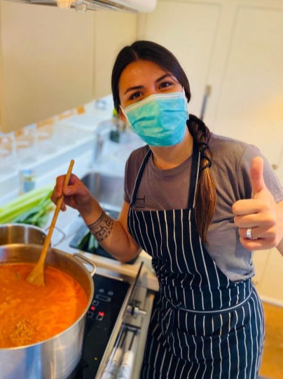 A woman in a galley cooking a soup and showing thumbs up