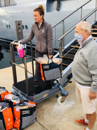 A man and a woman with bags of donations on a passerelle of a large yacht
