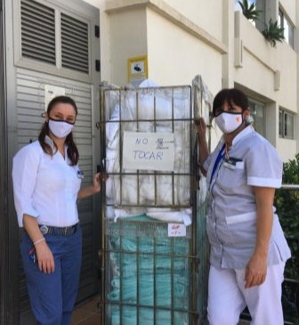 Two ladies next to a laundry trolley full of donated bedlinen from a hotel