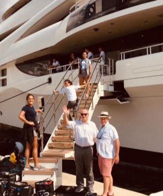 People waving on the dock alongside a large motor yacht