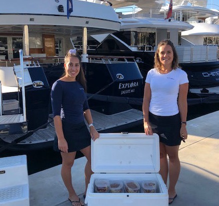 Two women standing on the dock with a cooler filled with food rations