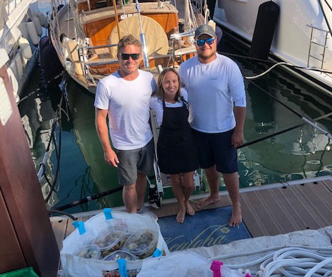 A chef and two deckhands standing on dock behind the boat with a full bag of food rations