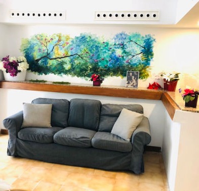 A grey sofa in the corner with a green mural on the wall behind it