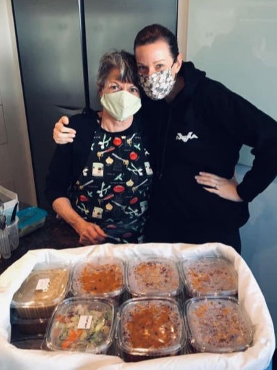Two women embracing in a galley behind a basket full of ready made meals