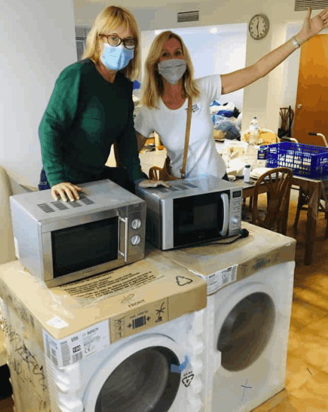 Two women behind two brand new washing machines and two microwave ovens